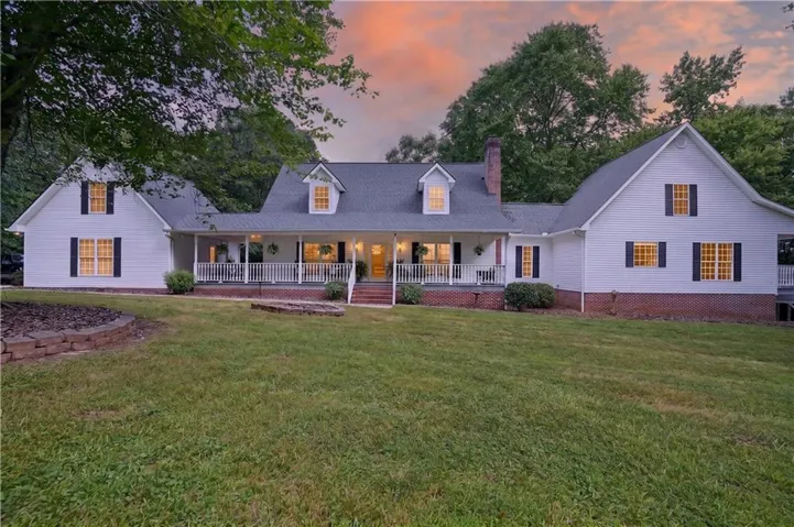 White exterior residence featuring a covered front porch with white railings, multiple dormer windows, black shutters, and an expansive lawn