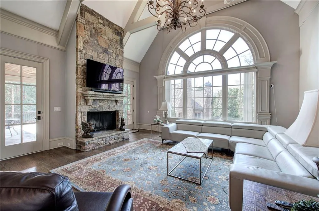 Living area featuring high vaulted ceiling, a chandelier, a stone fireplace, wood finished floors, and plenty of natural light