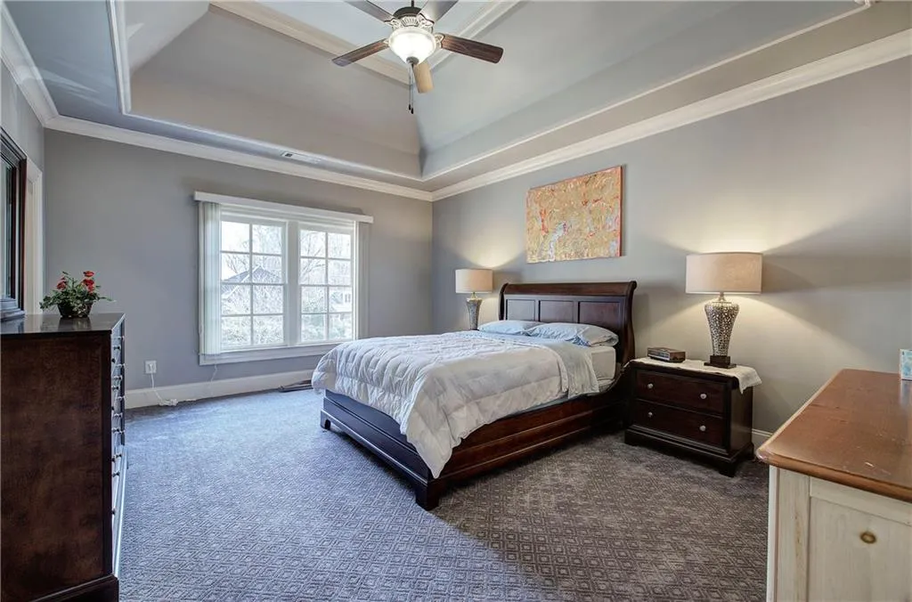 Bedroom with ornamental molding, a raised ceiling, dark colored carpet, and ceiling fan
