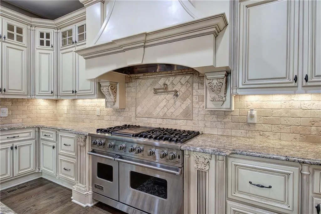 Kitchen with double oven range, light stone countertops, custom exhaust hood, and glass insert cabinets