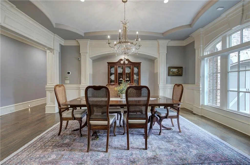 Dining space featuring ornate columns, wood finished floors, a chandelier, a tray ceiling, and a decorative wall
