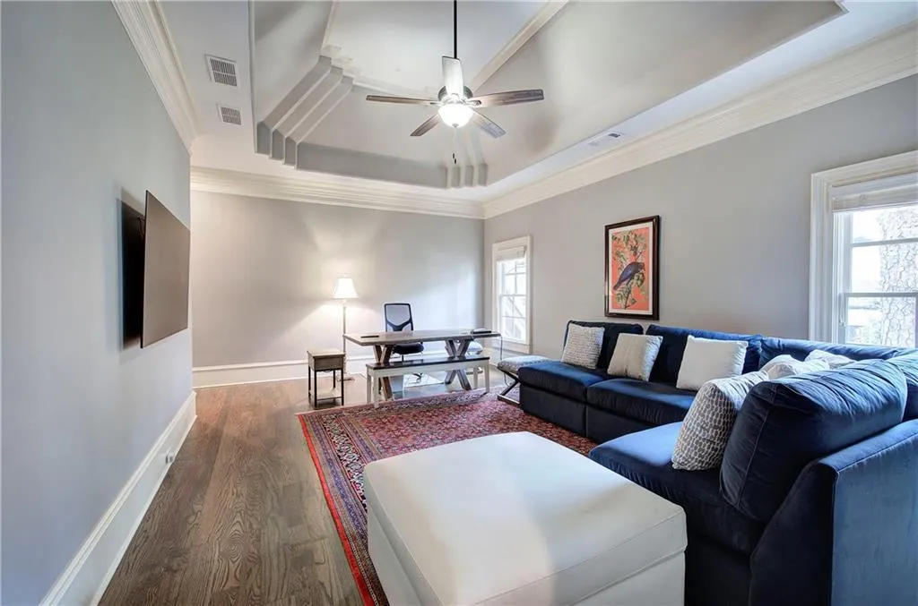 Living area with dark wood finished floors, a ceiling fan, a tray ceiling, and ornamental molding