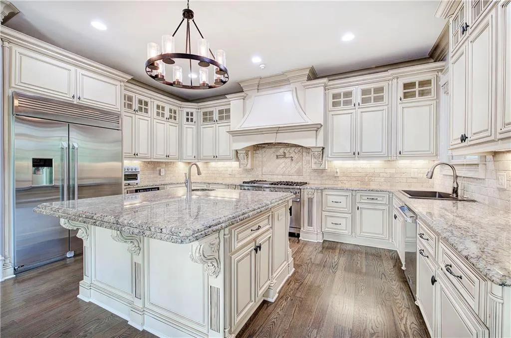 Kitchen featuring high end appliances, decorative light fixtures, light stone counters, a kitchen island with sink, and dark wood finished floors