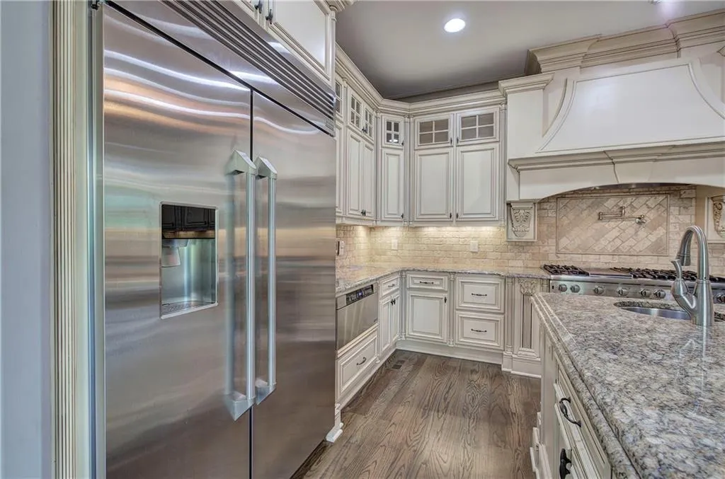 Kitchen with stainless steel appliances, glass insert cabinets, light stone counters, dark wood finished floors, and custom exhaust hood