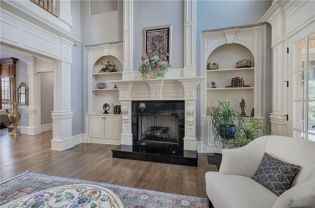 Living room featuring built in shelves, a towering ceiling, a fireplace with raised hearth, and dark wood-style flooring