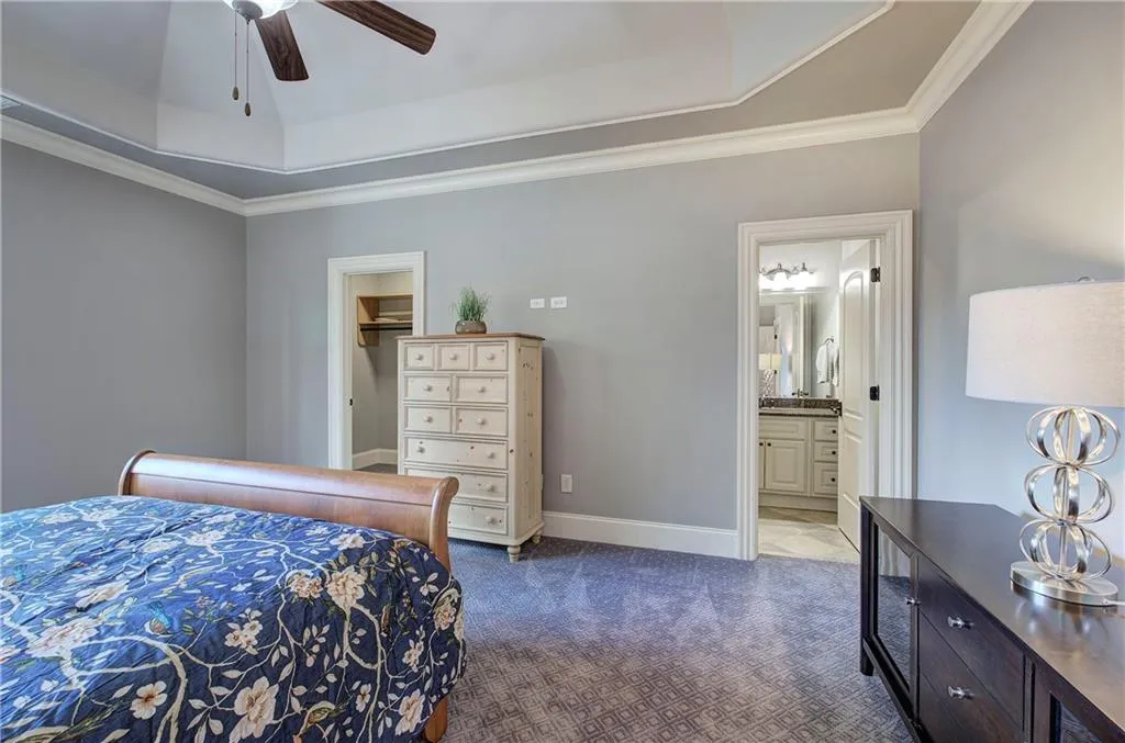 Bedroom with a tray ceiling, a spacious closet, dark colored carpet, crown molding, and a ceiling fan