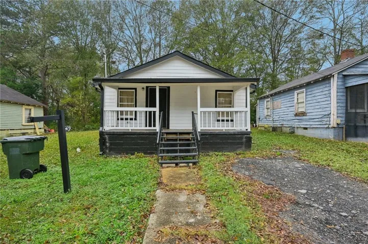 Single-story residence featuring white siding, a covered porch with white railing, and a dark-toned foundation