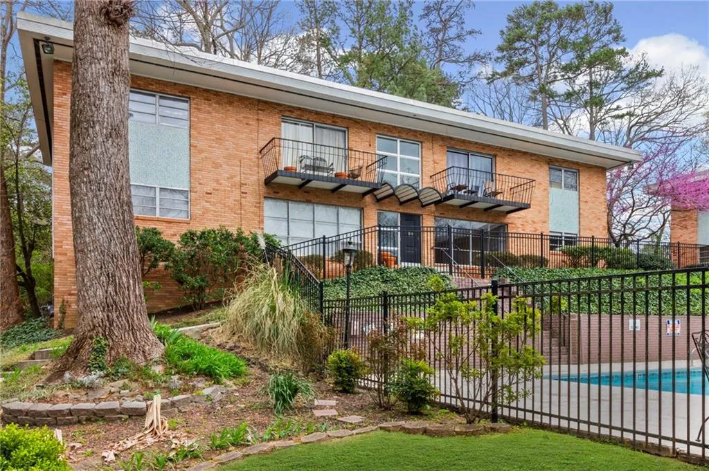 Back of property featuring a community pool, brick siding, a balcony, and fence