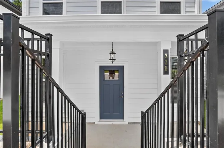 Inviting front entrance featuring a dark blue paneled door with upper glass inserts, flanked by a contemporary pendant light fixture and clear house numbering