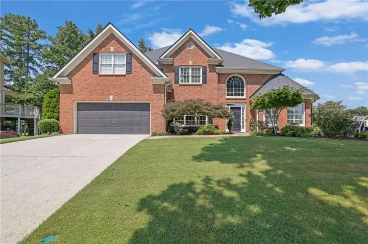 Traditional brick exterior featuring a two-car garage, manicured lawn, and mature landscaping