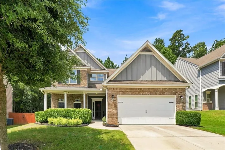 Two-story exterior featuring brick and siding accents, a covered front porch with white columns, a two-car garage with an asphalt driveway, and manicured landscaping