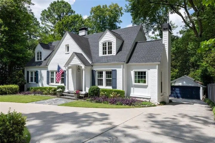 White brick exterior with a dark shingle roof, blue shutters, and a covered portico entry