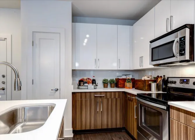 Kitchen with tasteful backsplash, dark hardwood / wood-style flooring, sink, white cabinetry, and appliances with stainless steel finishes