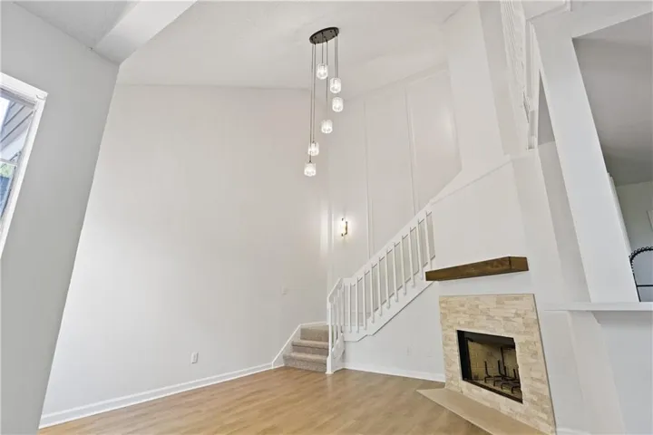 Vaulted ceiling with a multi-light pendant fixture, wood-finish flooring, staircase with white railing, and a fireplace featuring a natural stone facade and wood mantel