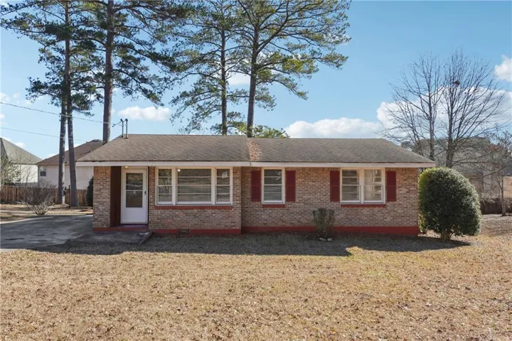 Brick exterior featuring red shutters, white frame windows, a covered entry, and mature trees