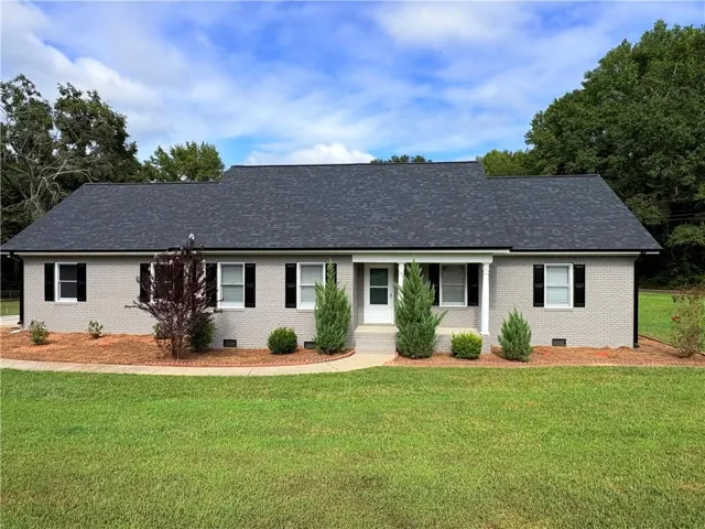 Brick exterior with a dark shingle roof, complemented by a covered front entry, and front landscaping with mature shrubs