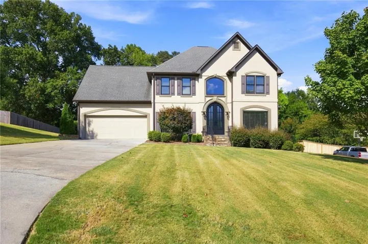 Stucco exterior with dark trim accents, a two-car garage, an arched front entry, and a mature tree-lined perimeter