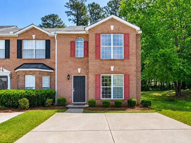 Brick exterior with red and black shutters, a concrete driveway, and mature landscaping
