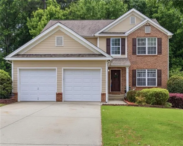 Traditional two-story residence featuring a brick and siding exterior, a two-car garage with white doors, a concrete driveway, and established front landscaping