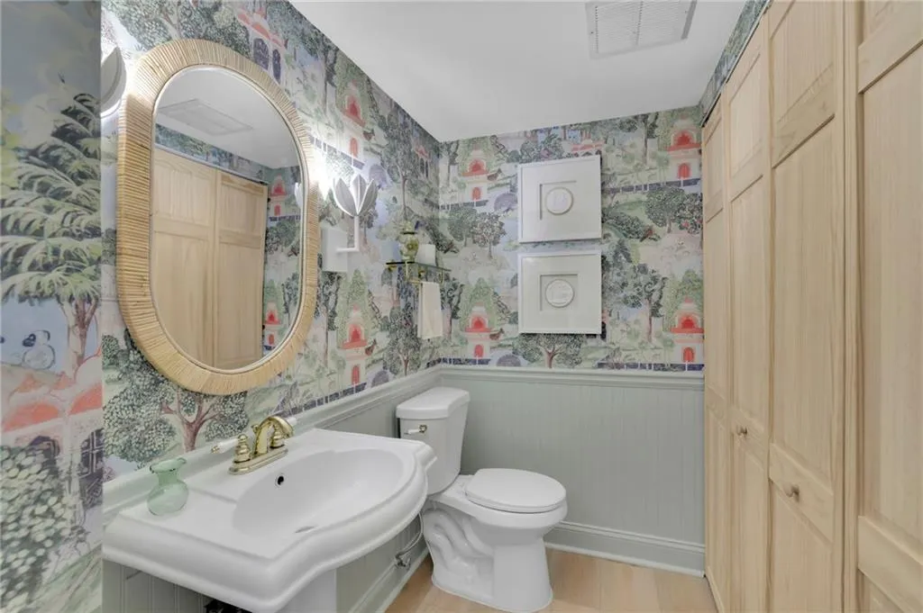 Bathroom with wallpapered walls, wainscoting, and light wood-style floors