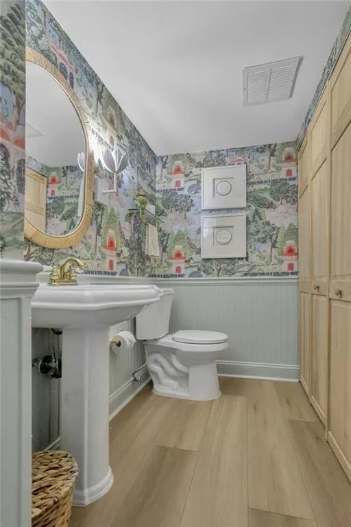 Bathroom with wallpapered walls, a wainscoted wall, and light wood-style floors
