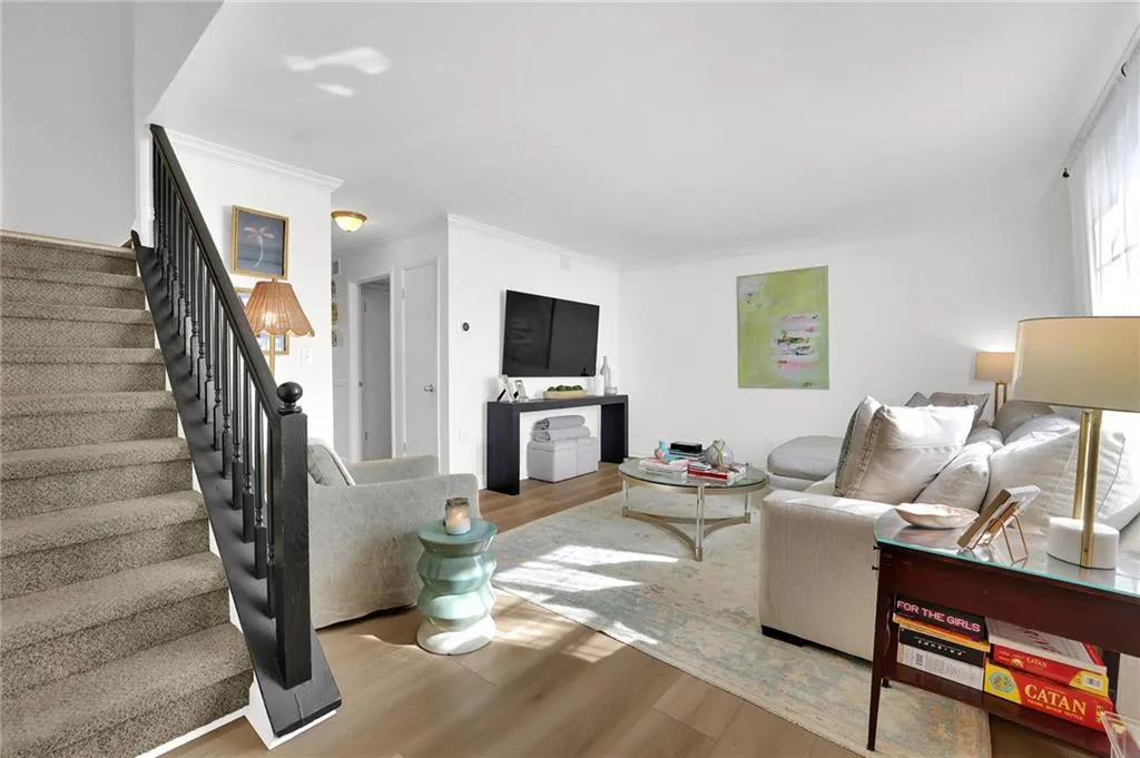 Living room with wood finished floors, stairs, and ornamental molding