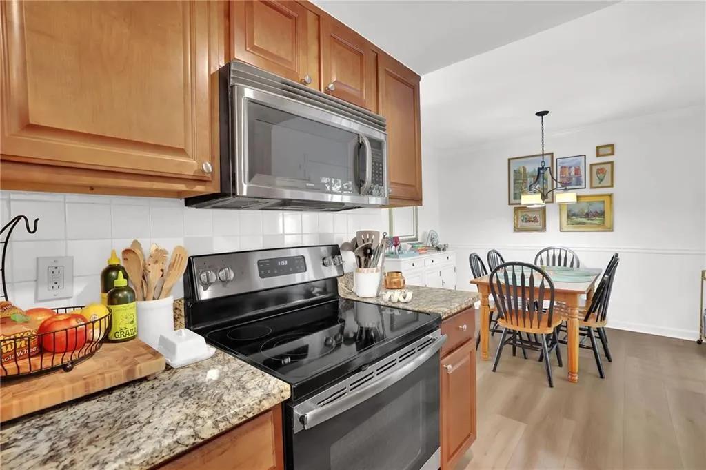 Kitchen with appliances with stainless steel finishes, light stone counters, tasteful backsplash, pendant lighting, and brown cabinets