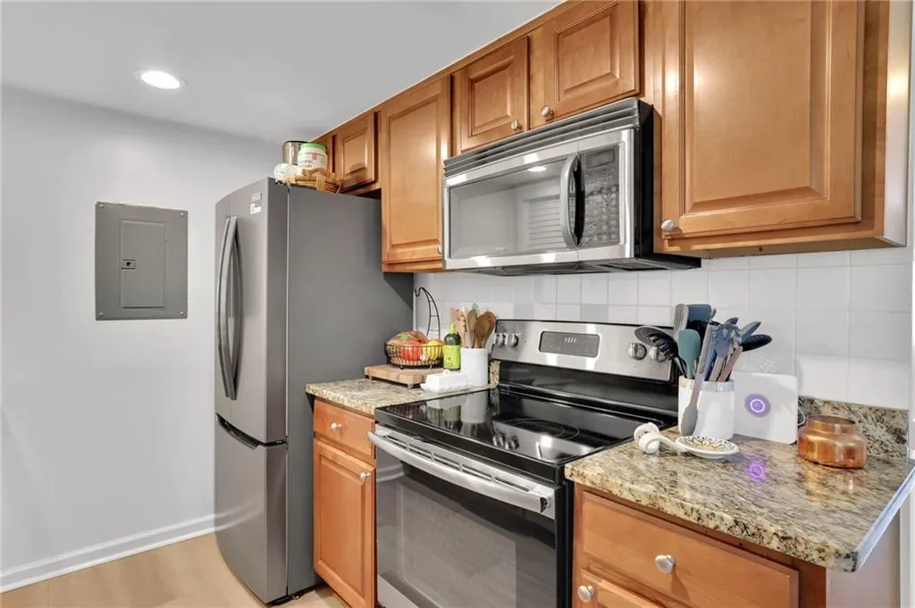 Kitchen with stainless steel appliances, light stone counters, tasteful backsplash, brown cabinetry, and recessed lighting