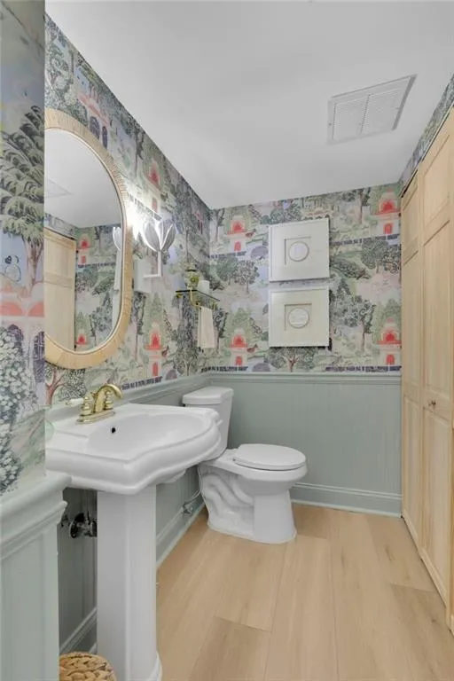 Half bath with wallpapered walls, wainscoting, and light wood-style floors