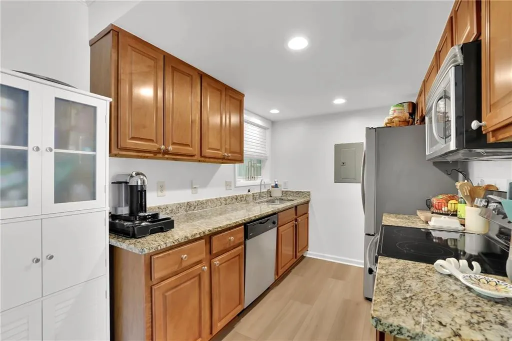 Kitchen with light stone countertops, brown cabinets, appliances with stainless steel finishes, recessed lighting, and light wood-style flooring