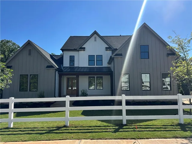 Contemporary farmhouse-style exterior with board and batten siding, multiple gables, a covered entry, and a white three-rail fence