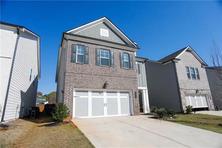 Brick Colonial two-story home featuring a three-car garage with white panel doors, gabled roofline with architectural detail, and a poured concrete driveway
