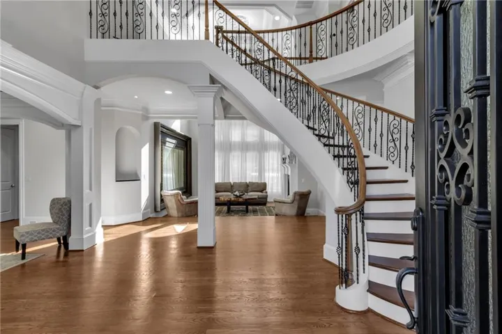 Entrance foyer featuring a high ceiling, wood finished floors, crown molding, arched walkways, and ornate columns