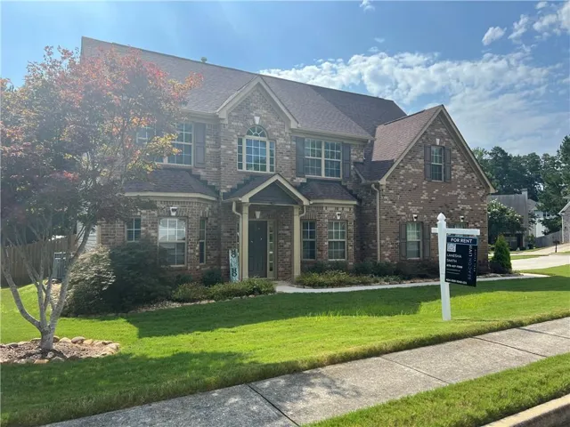 Brick facade residence with a brown shingle roof, arched and rectangular windows, and a covered entry