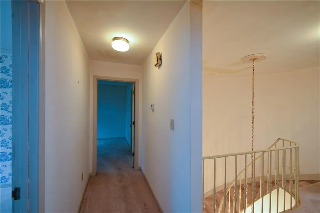 Corridor featuring light colored carpet and a notable chandelier