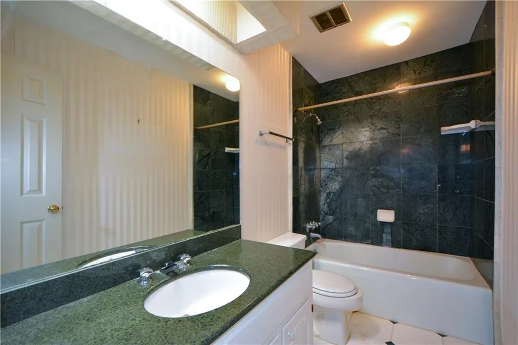 Full bathroom with tile flooring, oversized vanity, tiled shower / bath combo, and toilet