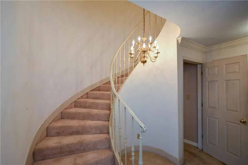 Stairs with an inviting chandelier, ornamental molding, and carpet