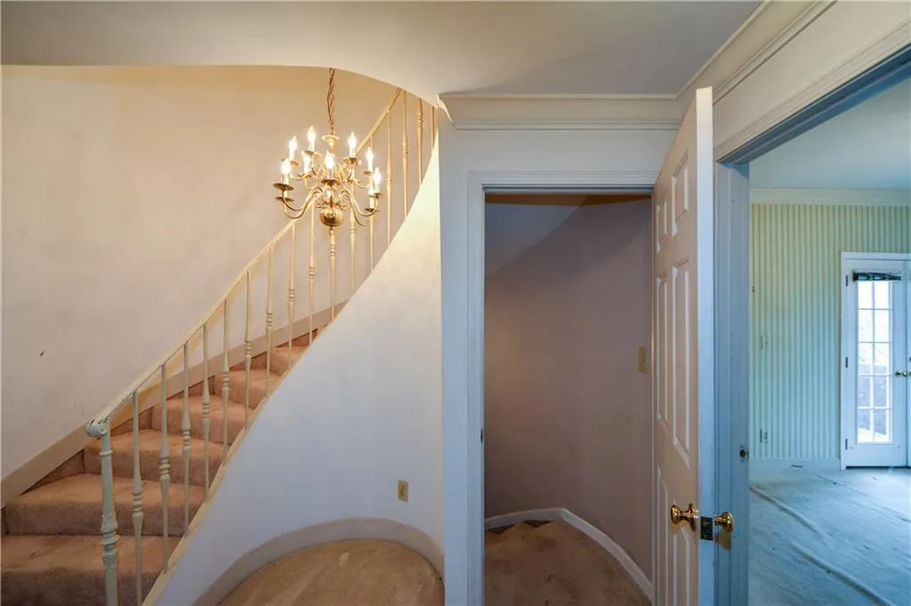 Stairs with a notable chandelier, light carpet, and ornamental molding