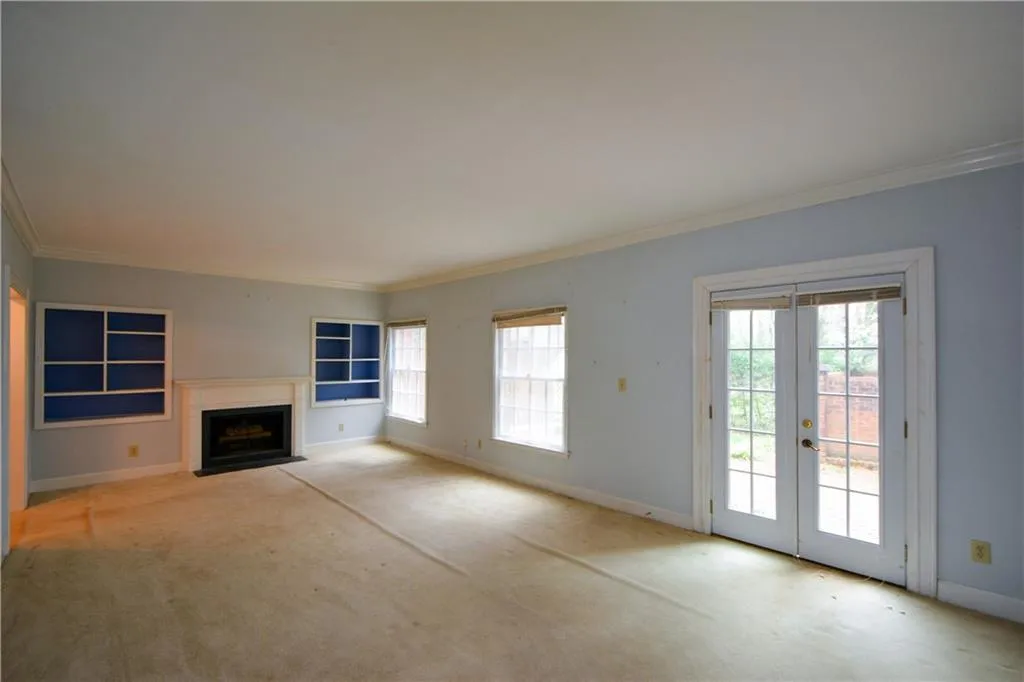 Unfurnished living room featuring french doors, crown molding, a wealth of natural light, and light carpet