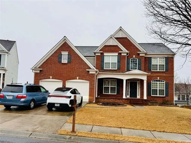 Brick exterior with white trim accents and dark shutters, featuring a covered front entry, twin gables, and an attached two-car garage