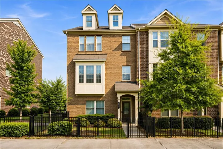 Brick exterior with decorative dormers, bay window, covered entryway, and a black wrought iron fence