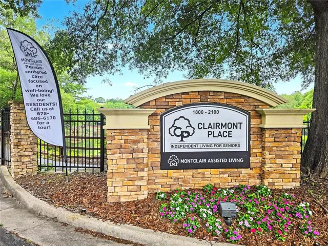 Clairmont Place Senior Living Community entrance featuring welcoming brick pillars with arched architectural detailing, professional signage, and mature landscaping with flowering plantings and established trees providing natural shade and curb appeal