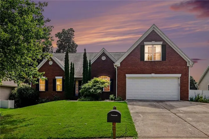 Brick exterior with white trim, attached garage with a white door, concrete driveway, and a manicured lawn