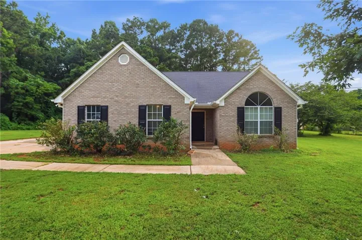 Brick exterior residence featuring a dark shingle roof, arched transom window, black louvered shutters, and a concrete pathway leading to the front entry