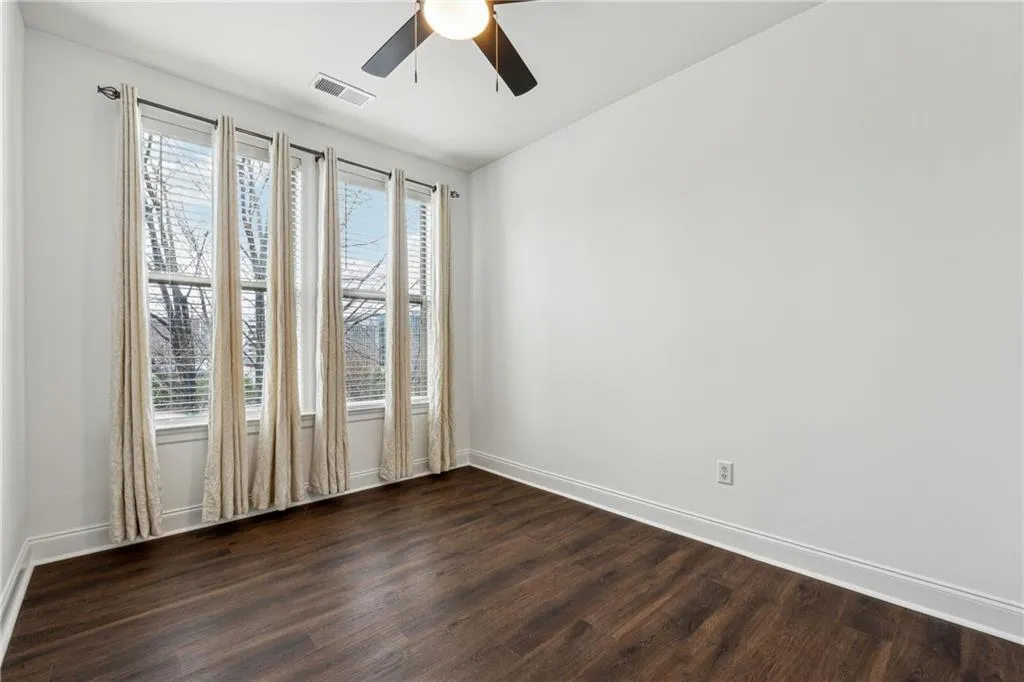 Empty room featuring a wealth of natural light, dark wood-style floors, and ceiling fan