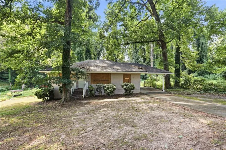 Single-story residence featuring a covered entry, concrete driveway, and mature trees
