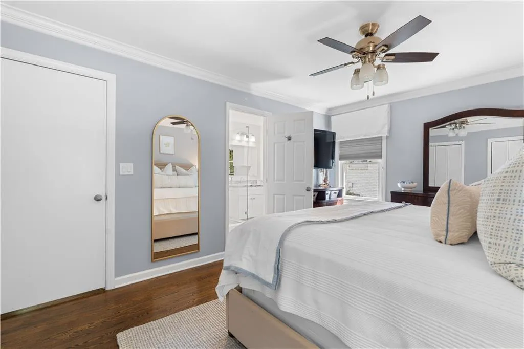 Bedroom featuring dark wood-type flooring, crown molding, ceiling fan, and ensuite bathroom