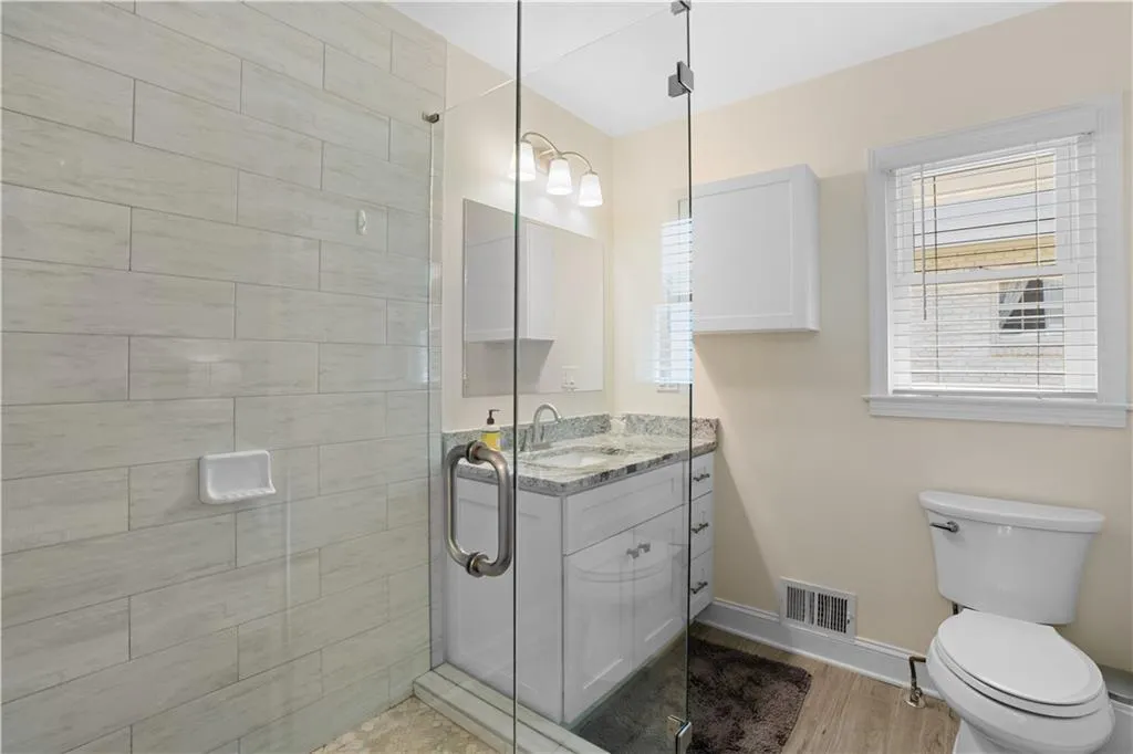 Bathroom with toilet, vanity, hardwood / wood-style flooring, and a shower with door