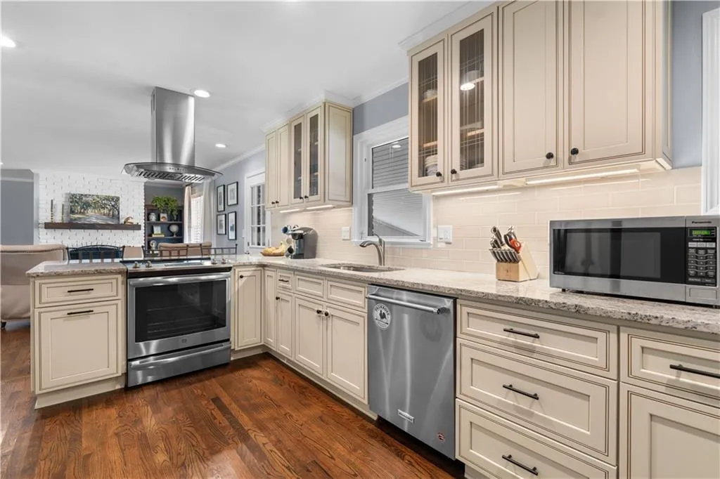 Kitchen featuring appliances with stainless steel finishes, crown molding, dark wood-type flooring, island exhaust hood, and cream cabinetry
