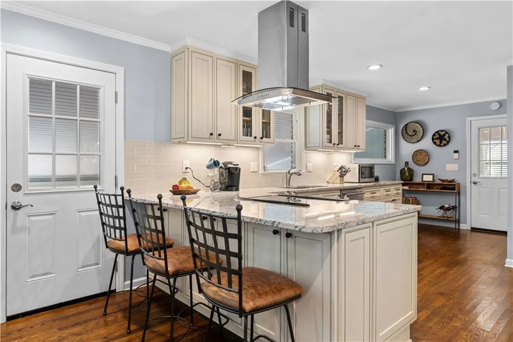 Kitchen with a kitchen bar, dark wood-type flooring, light stone counters, island range hood, and ornamental molding